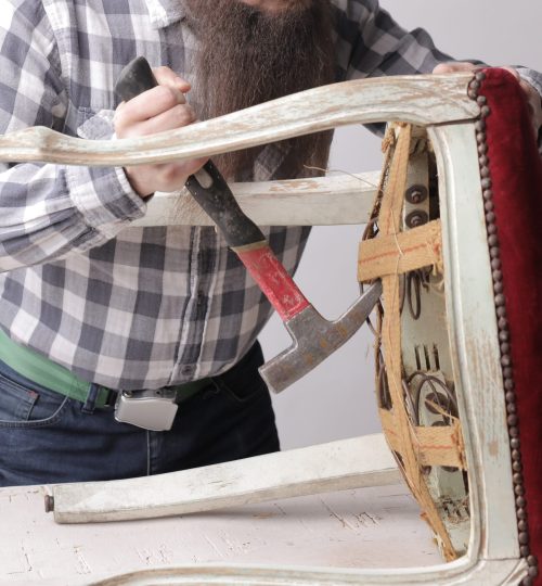 A vertical shot of a man with a long beard and a mustache fixing a broken chair